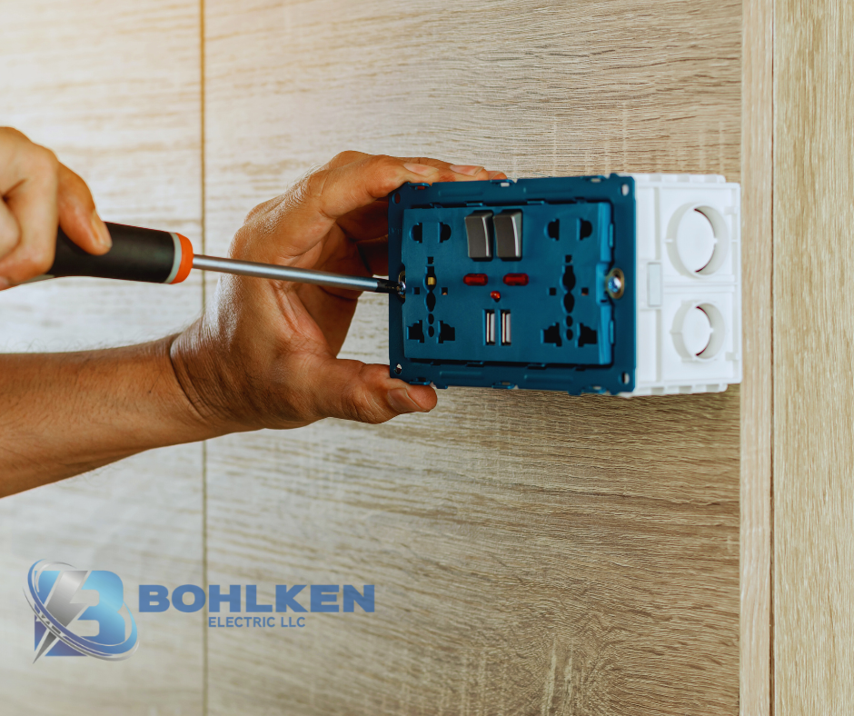 Bohlken Electric Electrician fixes a wall outlet with a screwdriver on wood paneling in Mount Vernon TX. Bohlken Electric LLC logo shown bottom left. Mount Vernon TX Electrician