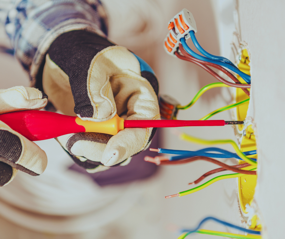 Bohlken Electric Bohlken Electric technician with gloves uses screwdriver on exposed wires in a Mount Vernon TX wall socket, fixing electrical issues. Mount Vernon TX Electrician
